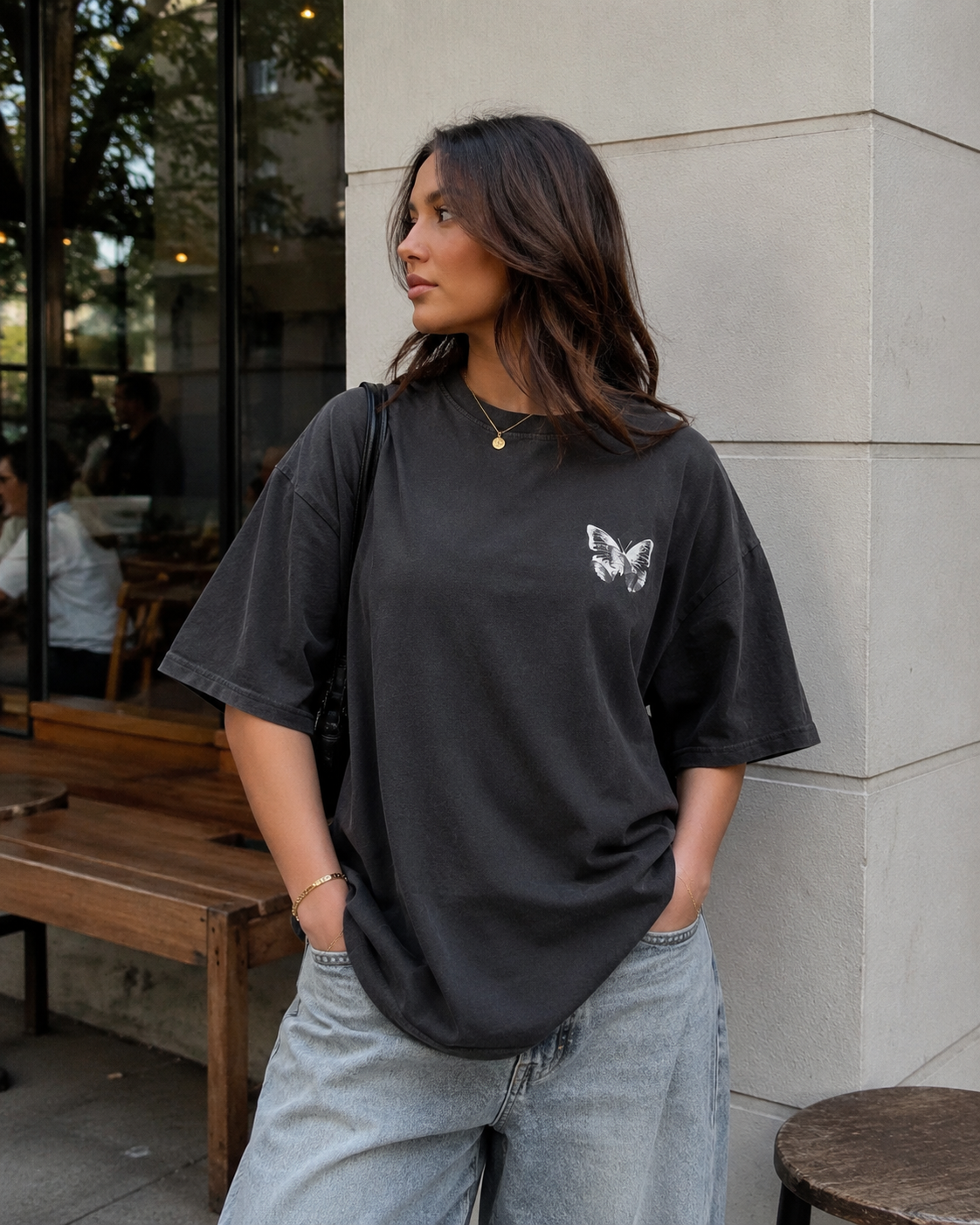 Person wearing a black t-shirt with a butterfly design, standing against a building exterior.