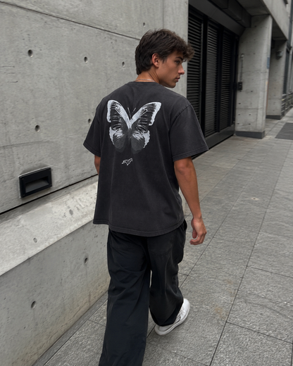 Person wearing a black t-shirt with a butterfly design walking on a sidewalk.
